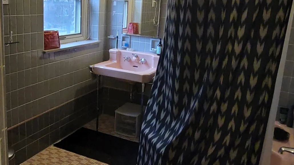 Before photo of an outdated Chicago bathroom featuring vintage pink wall tiles and an original bathtub prior to renovation.