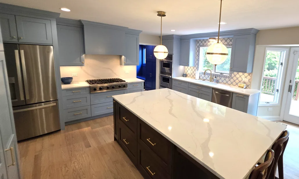 Modern kitchen remodel in Hinsdale, IL featuring blue shaker cabinets, a large quartz waterfall island, stainless steel appliances, custom backsplash tile, and open-concept kitchen design by Maya Construction Group.
