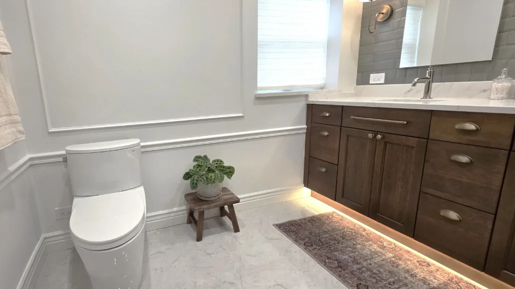 A beautifully updated bathroom featuring a dark wood vanity with under-cabinet lighting, wainscoting wall panels, and a sleek modern toilet completed by Maya Construction.